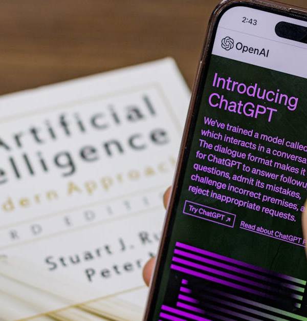 Close-up of a smartphone displaying ChatGPT app held over AI textbook.