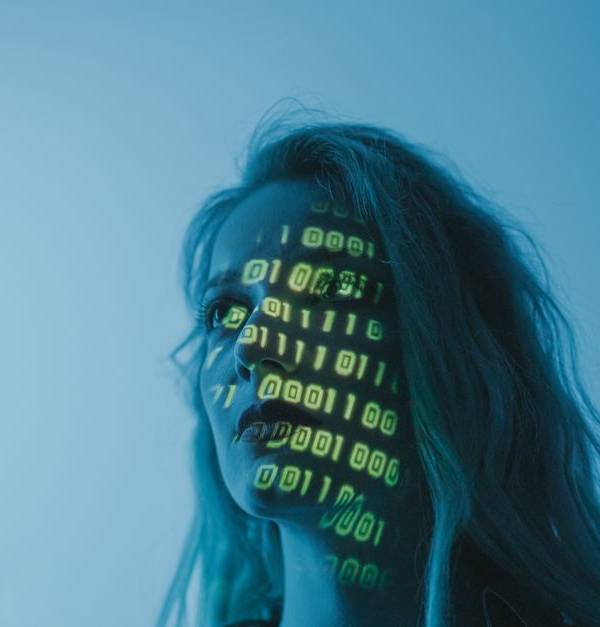 A woman with binary code lights projected on her face, symbolizing technology.