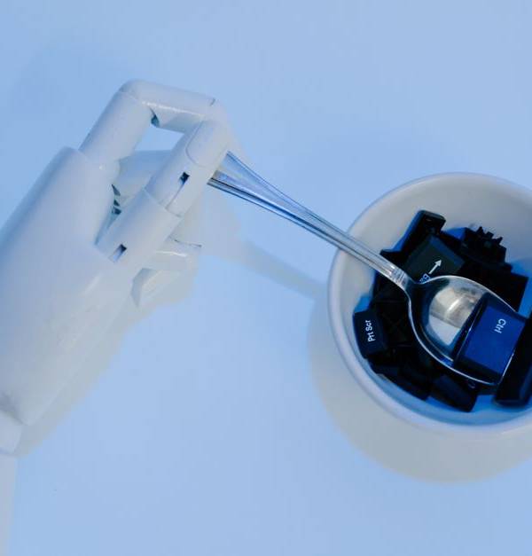 A robotic hand holds a spoon filled with keyboard keys, symbolizing AI and technology fusion.