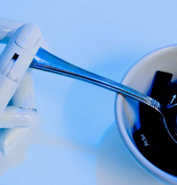 A robotic hand holding a spoon above a bowl with keyboard keys, showcasing technology themes.