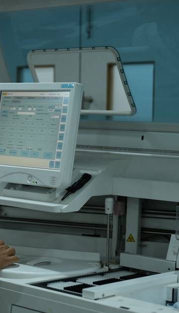 A lab technician operates a clinical analyzer in a modern laboratory setting.