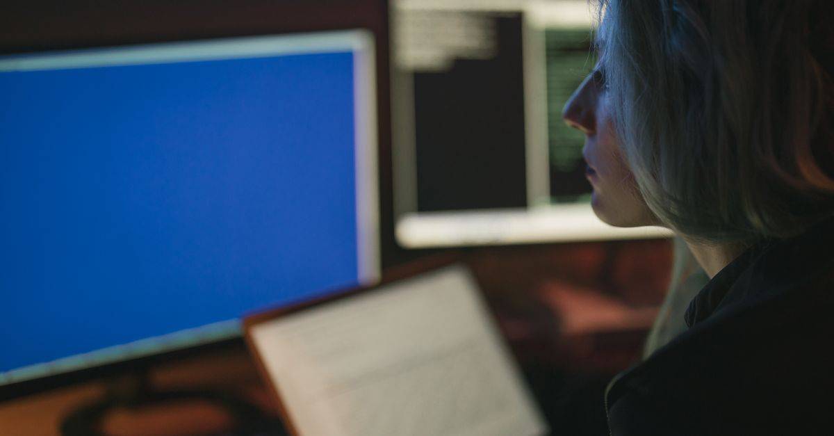 A woman working on multiple computer screens at night, focusing on her tasks.