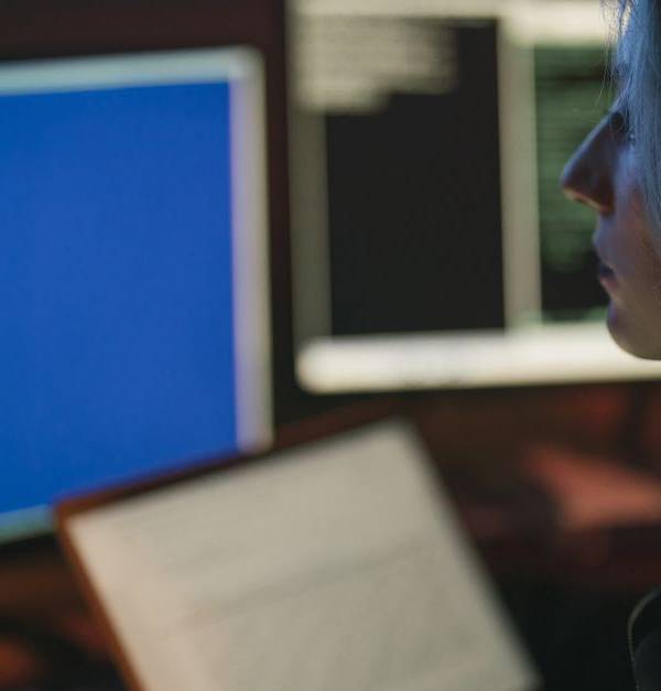 A woman working on multiple computer screens at night, focusing on her tasks.