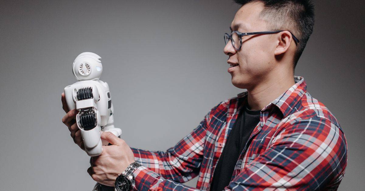 Asian man with glasses in plaid shirt holding a robot toy indoors. Studio shot.