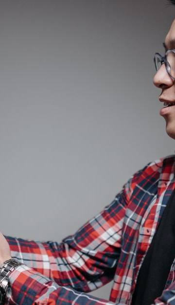 Asian man with glasses in plaid shirt holding a robot toy indoors. Studio shot.