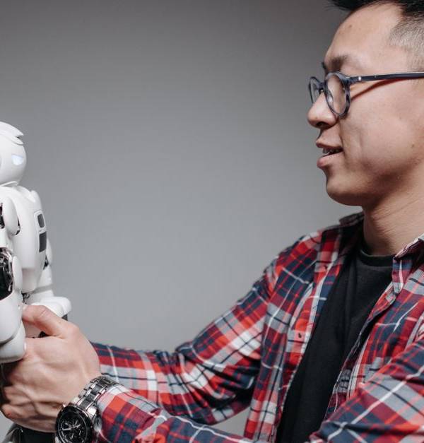 Asian man with glasses in plaid shirt holding a robot toy indoors. Studio shot.