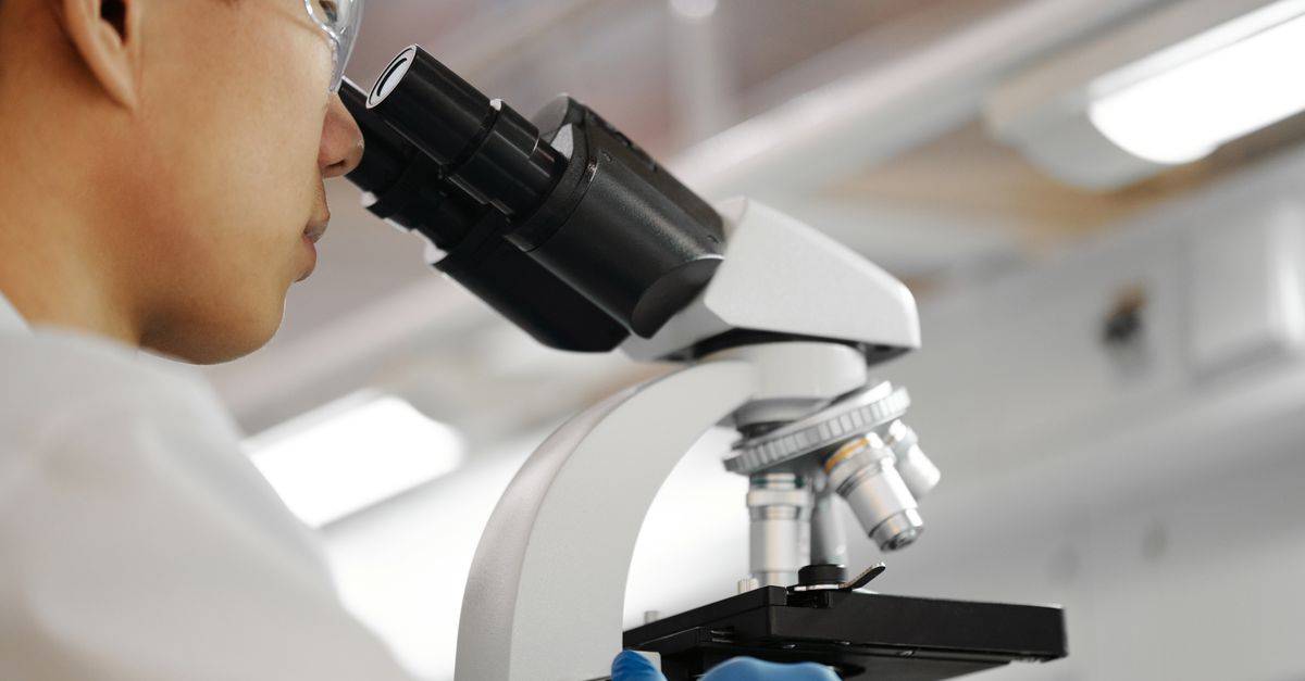 Male scientist studies samples under microscope in modern laboratory setting.