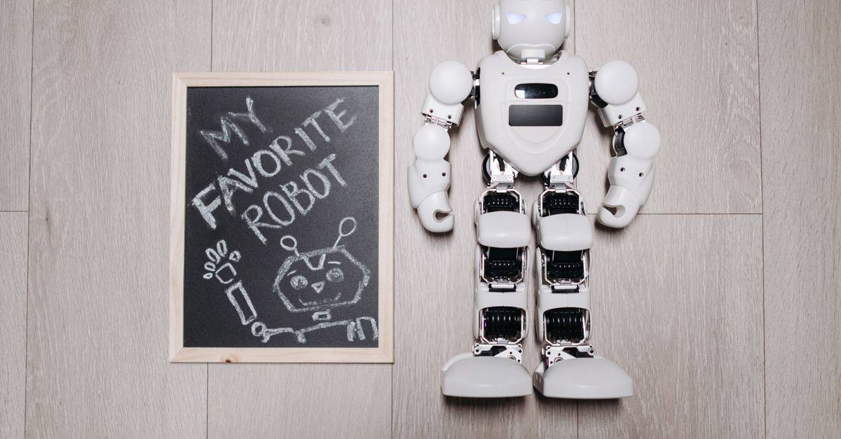 Overhead shot of a robot toy alongside a chalkboard drawing, on a light wooden floor.