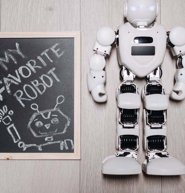 Overhead shot of a robot toy alongside a chalkboard drawing, on a light wooden floor.