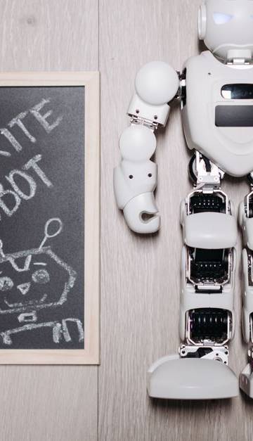 Overhead shot of a robot toy alongside a chalkboard drawing, on a light wooden floor.