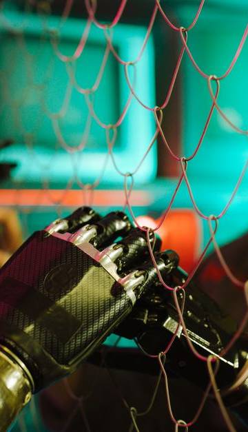 A woman interacts with robotic hands through a mesh displaying a neon cyberpunk atmosphere.