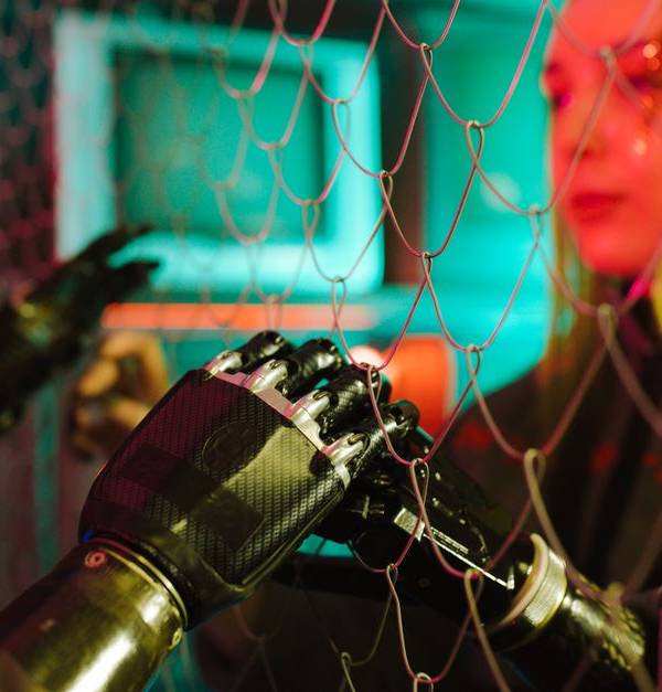A woman interacts with robotic hands through a mesh displaying a neon cyberpunk atmosphere.