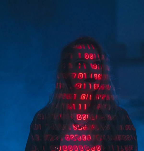 A mysterious silhouette with red binary code projected over the face, set against a dark, moody background.