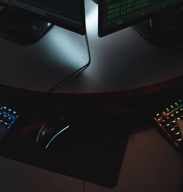 Two people typing on RGB keyboards with code on screens, indicating a cybersecurity environment.