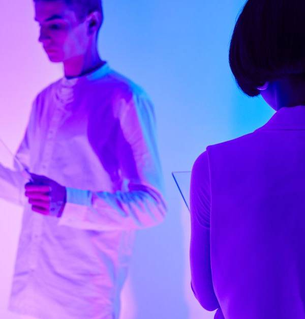 Two individuals interact with digital interfaces in a colorful futuristic setting.