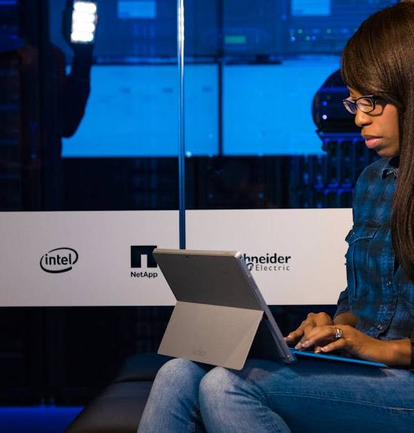 Professional woman working on laptop in a server room, showcasing technology and remote work.