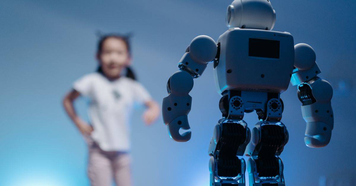 A young girl playfully interacts with a humanoid robot in a futuristic indoor environment featuring soft blue lighting.