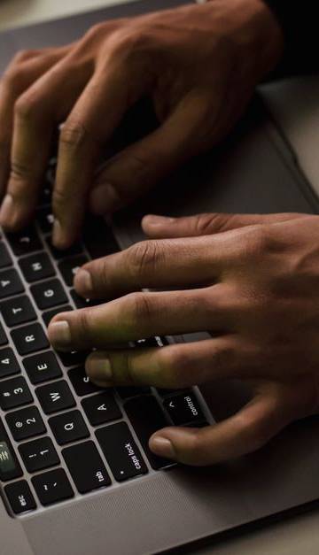 From above of crop anonymous male hacker typing on netbook with data on screen while sitting at desk