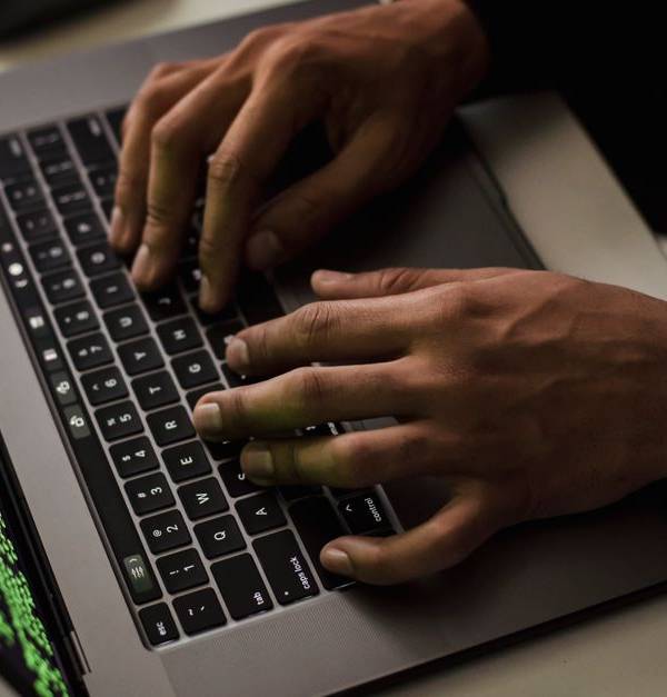 From above of crop anonymous male hacker typing on netbook with data on screen while sitting at desk