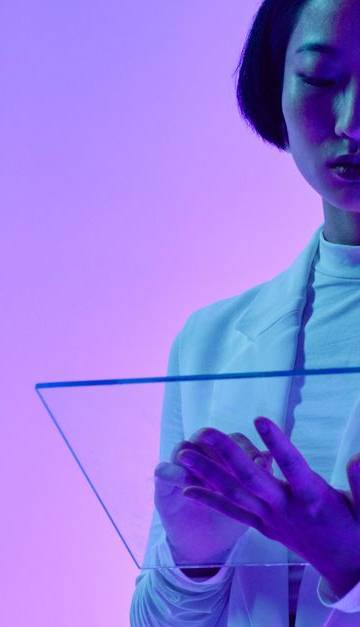 Woman interacts with a transparent digital screen in vibrant studio lighting.