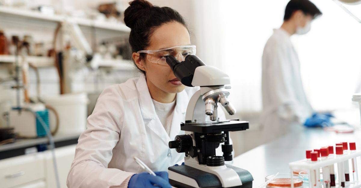 A scientist in a lab coat using a microscope in a modern laboratory setting.