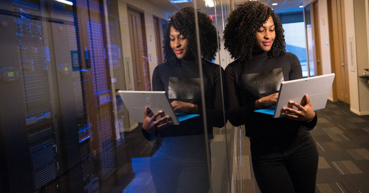 African American woman standing in modern office using laptop, reflecting professionalism and technology engagement.
