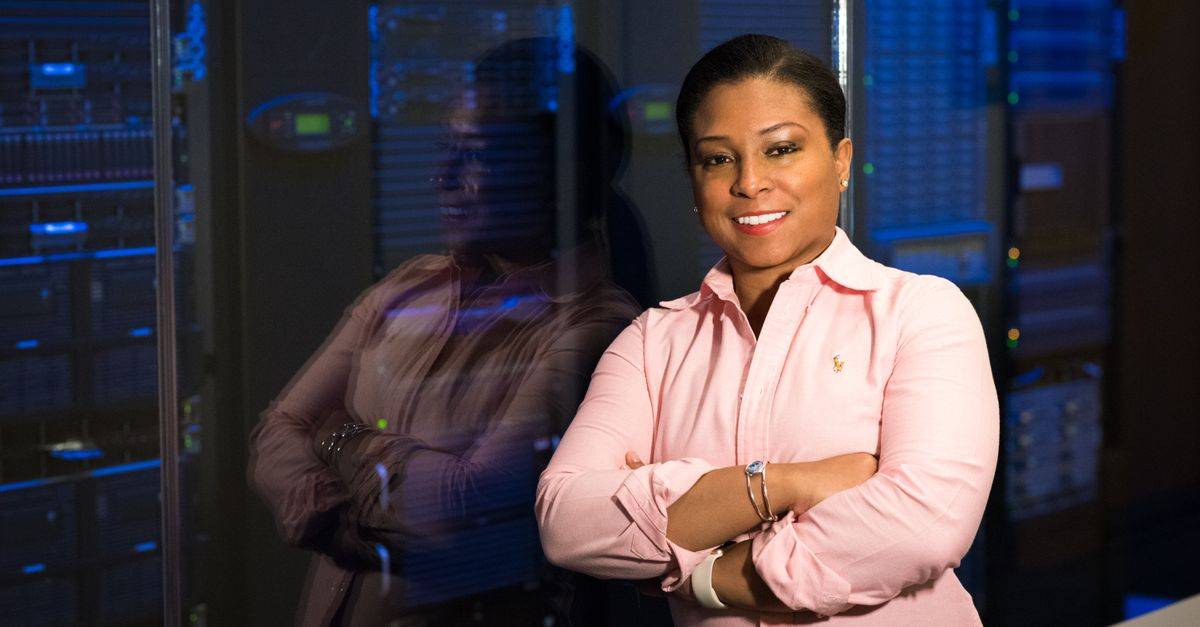 Smiling IT professional with crossed arms in a server room, reflecting her expertise.