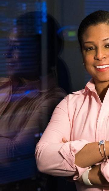 Smiling IT professional with crossed arms in a server room, reflecting her expertise.