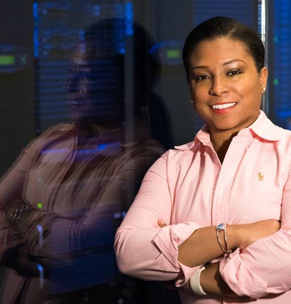 Smiling IT professional with crossed arms in a server room, reflecting her expertise.