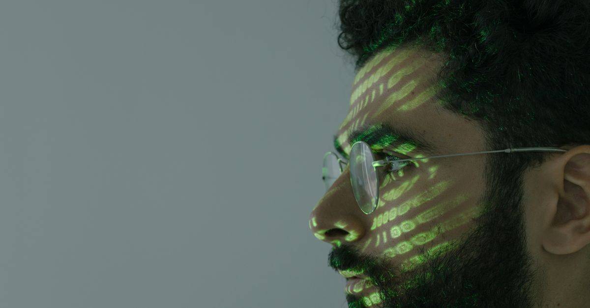 Side profile of a man with eyeglasses and green binary code projected on face.
