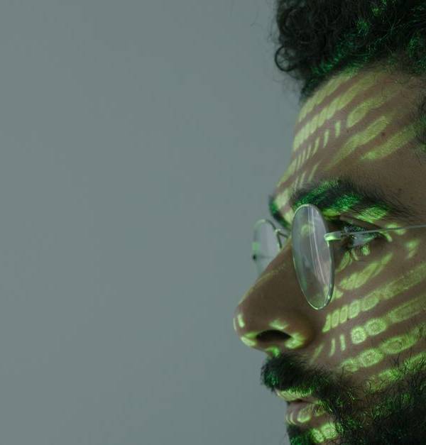 Side profile of a man with eyeglasses and green binary code projected on face.