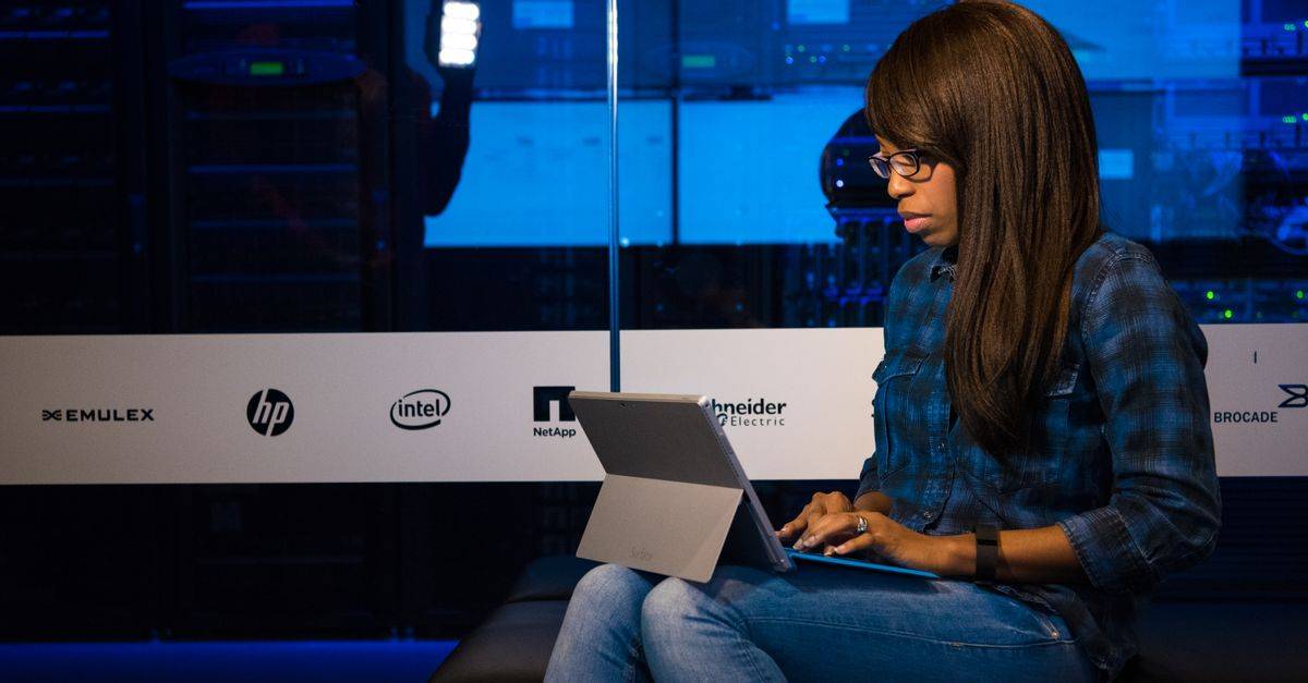 Professional woman working on laptop in a server room, showcasing technology and remote work.