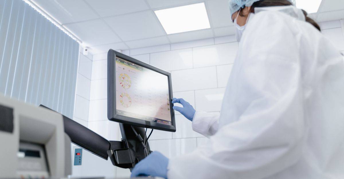 Woman in lab coat using touchscreen monitor in a modern laboratory setting.