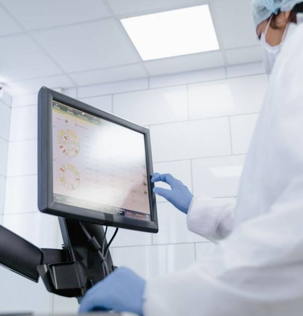 Woman in lab coat using touchscreen monitor in a modern laboratory setting.