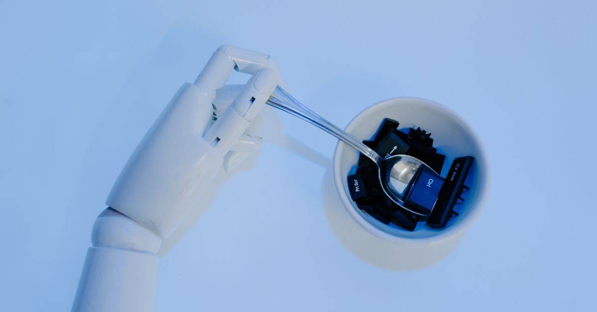 A robotic hand holds a spoon filled with keyboard keys, symbolizing AI and technology fusion.