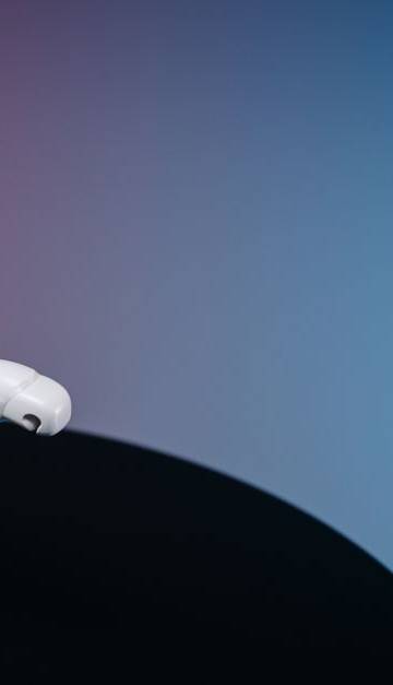 A white humanoid toy robot standing on a reflective black surface in a studio setting with a blue and pink gradient background.