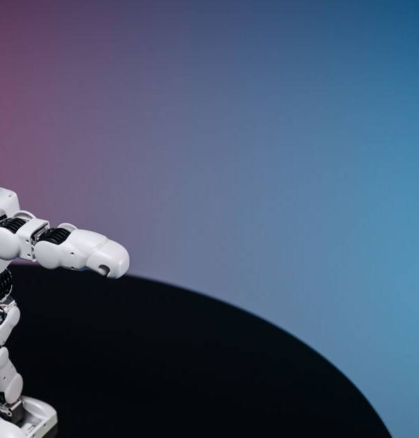 A white humanoid toy robot standing on a reflective black surface in a studio setting with a blue and pink gradient background.